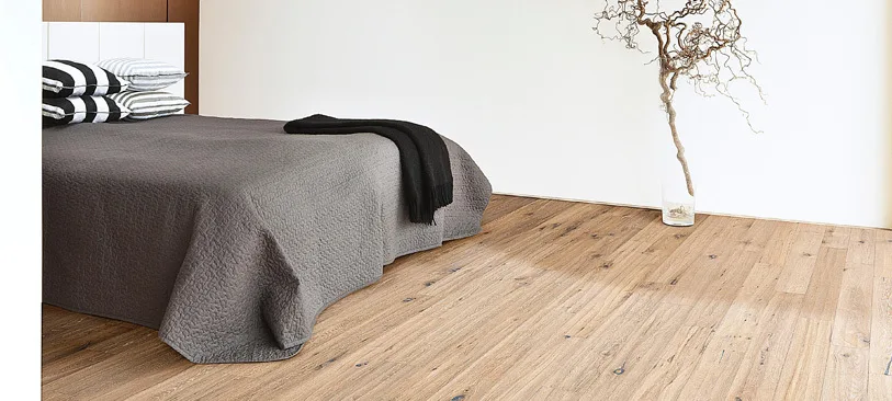 Schlafzimmer mit hellem Eichenparkett und grauem Bett